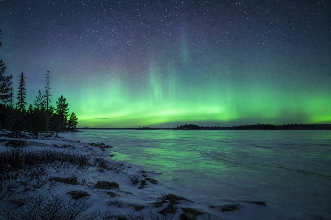 Vast flat frozen lake horizon at night with stars and a low green aurora glow all around