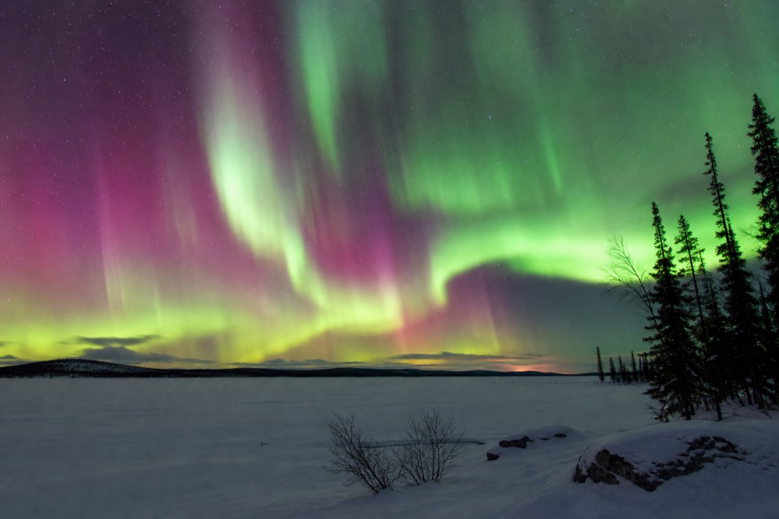 Bright multi-band aurora display filling the sky above a flat snow-covered lake horizon