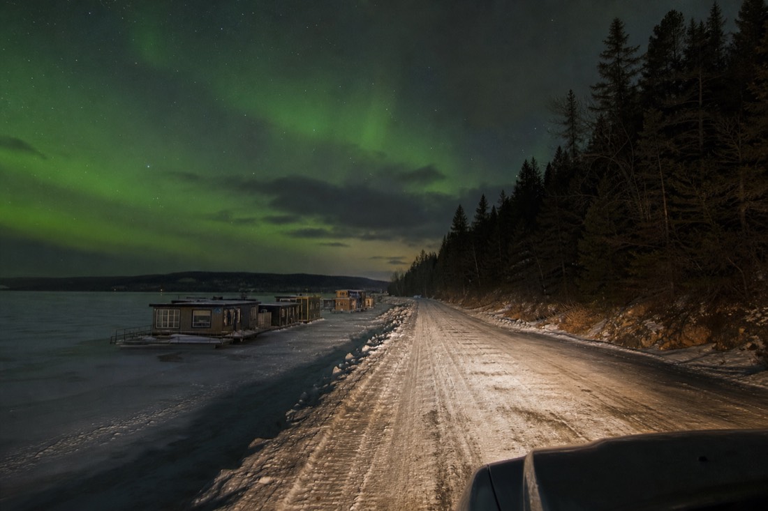 Car headlights on a plowed ice road crossing a frozen bay with houseboats frozen in along the shore